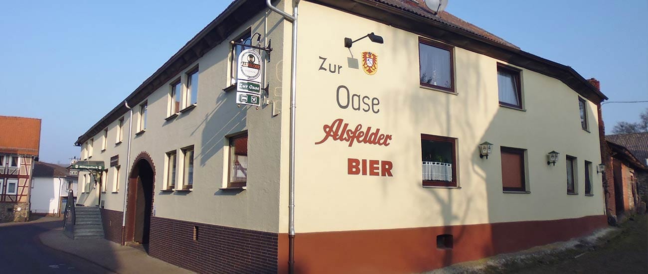 Außenansicht des Landhotels Zur Oase mit dem Schriftzug „Zur Oase – Alsfelder Bier“ an der Fassade