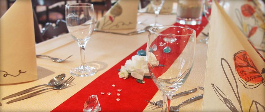 Festlich gedeckte Tafel mit Weingläsern, weißen Rosen und rotem Tischläufer