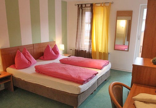 Doppelzimmer mit grün-weiß gestreifter Wand, Doppelbett und Holzmöbeln