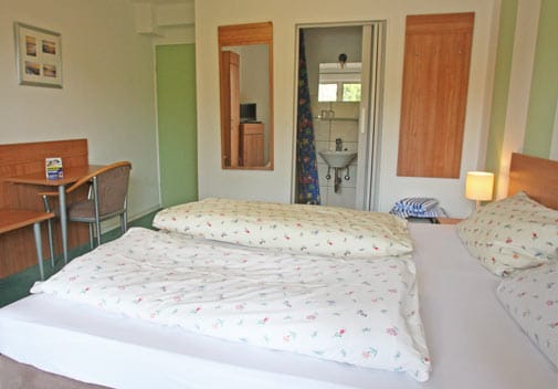 Doppelzimmer mit Doppelbett, Schreibtisch und Blick ins Bad